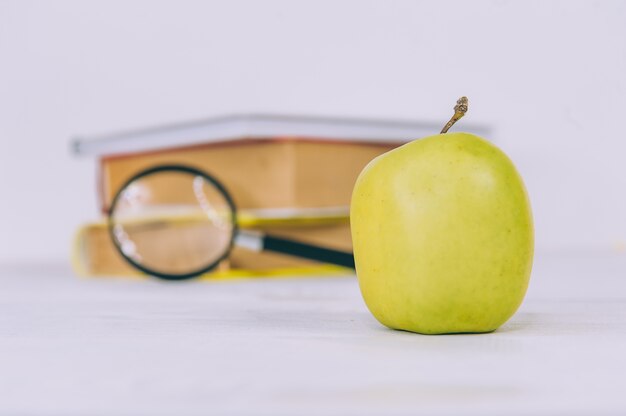 Concept Back to School. Green apple with magnifying glass on a space of books.