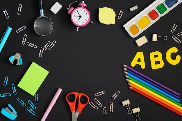 Concept, Back to school. A photo from above, on a black background lie multi-colored school and office supplies. In the center of an empty space for text or inscriptions.