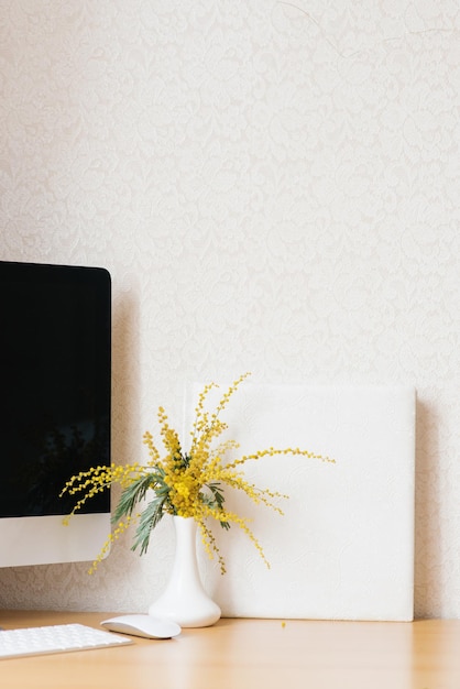 Concept of a business freelancer blogger The laptop is on a wooden table against a white wall with a mimosa in a vase