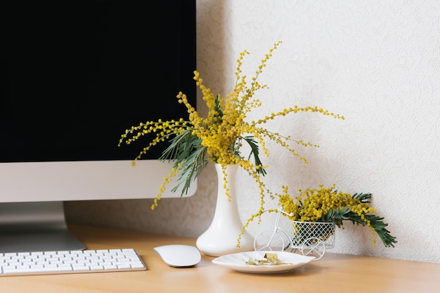 Concept of a business freelancer blogger The laptop is on a wooden table against a white wall with a mimosa in a vase