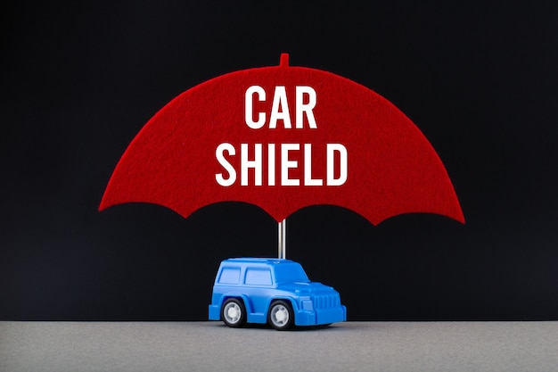 Photo concept of car insurance. blue car under red umbrella with text car shield.