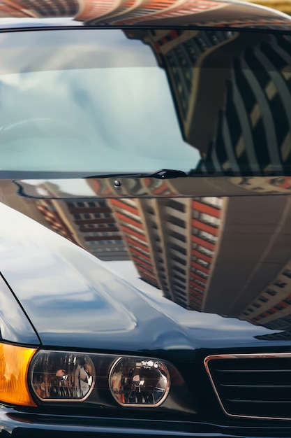 Concept of car in real world. Front of automobile close up. Blue sky reflected in metallic body and windshield of auto.