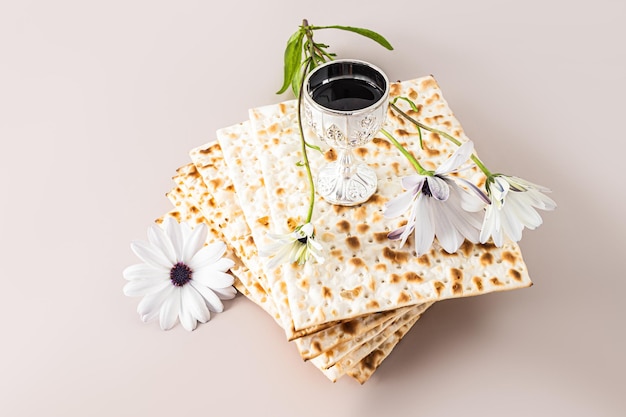 Concept of celebrating the Jewish holiday of Passover A stack of matza and a silver cup with red wine and a delicate flower Pastel background