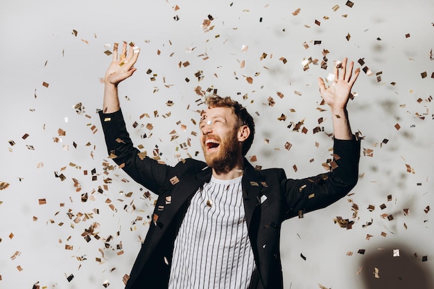 Concept of celebration and victory Stylish young man isolated on white background under glittering confetti