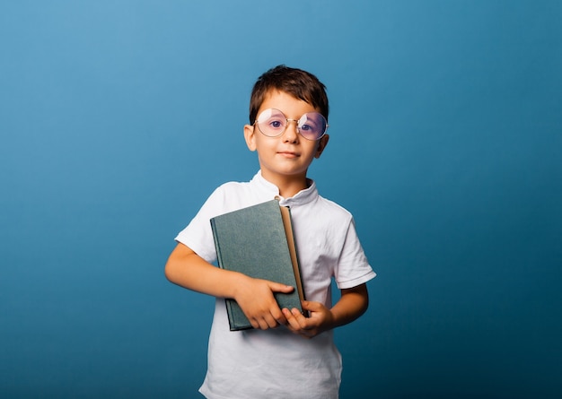 Concept of childhood, school, education and people - happy smiling boy with glasses holding a book.