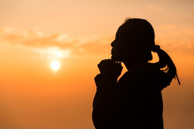 Concept Christian person worship or pray to God Christian woman silhouette with love faith devotion to God with sunrise sky background worship God for peace victory success with hope religion