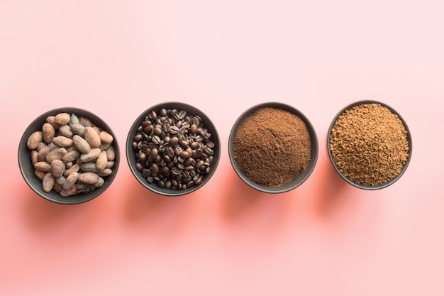 Concept of cocoa and coffee beans in bowls on pink background.