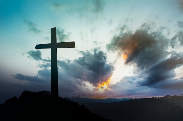 Concept conceptual black cross religion symbol silhouette in grass over sunset or sunrise sky