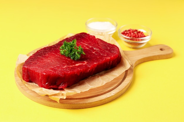 Concept of cooking with raw beef steak on yellow background