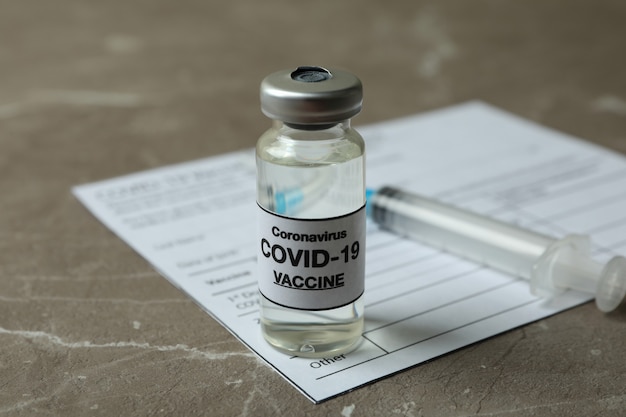 Concept of Covid - 19 vaccination with vaccine and syringe on gray textured table