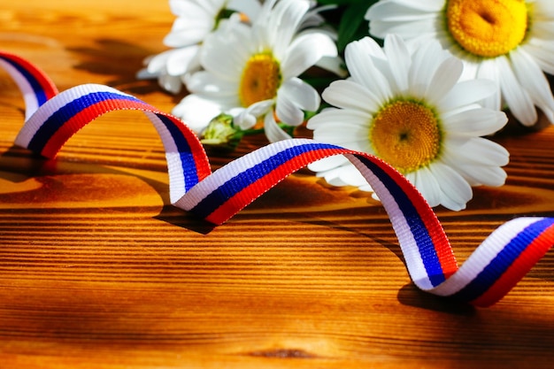 The concept of the Day of Russia The ribbon is painted in the colors of the Russian flag and a daisy on a wooden background