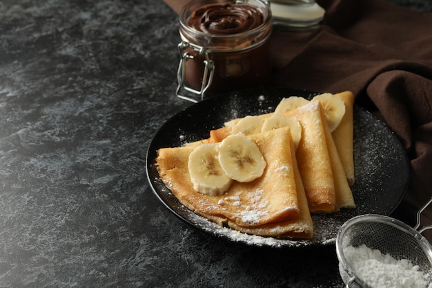 Concept of delicious breakfast with crepes with sugar powder and banana on black smokey background