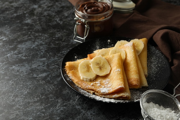 Concept of delicious breakfast with crepes with sugar powder and banana on black smokey surface