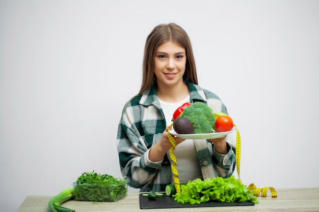 Concept of diet and healthy eating woman with vegetables on white wall background