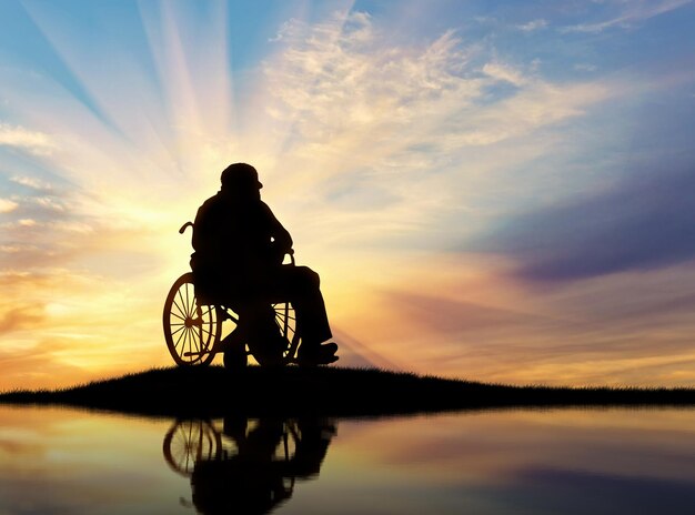 Concept of disability and old age. Silhouette of disabled person in a wheelchair at sunset and reflection in water