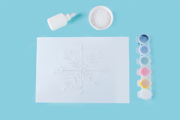 Concept of DIY and kid's creativity. Step by step instruction: how to make snowflake from glue and salt on paper. Step 3 child's hands apply glue to drawing.