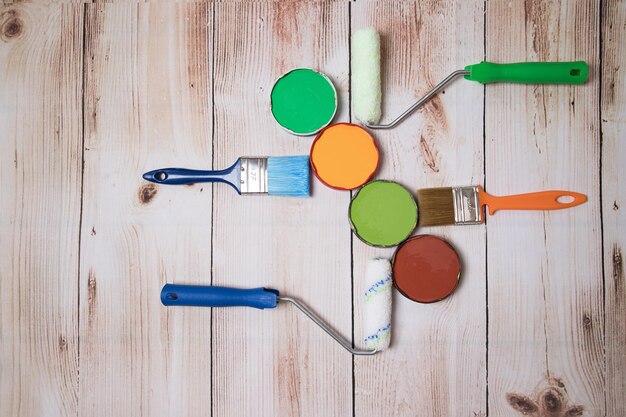 The concept of DIY repair Paints brushes and paint rollers are laid out on a wooden background