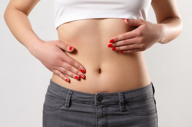 Concept of early term of pregnancy. Close up photo of woman's abdomen and belly button, she is touching her slim stomach with two hands. isolated white wall