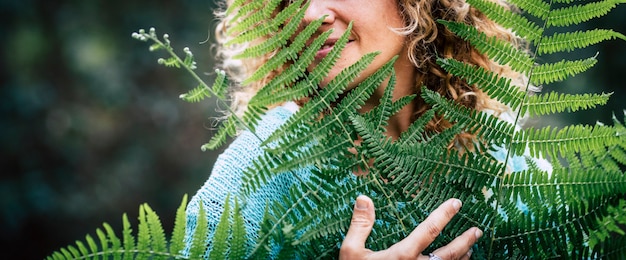 Concept of earth's day love and celebration with closeup portrait of smiling adult woman hugging a big tree leaf in outdoor nature forest