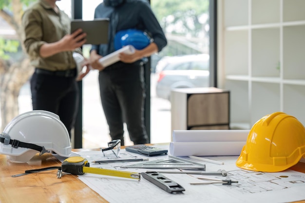 Concept of engineering equipments of protective helmet for competent engineer on piles of paper works Blurred image of engineer working together at the desk