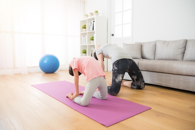 concept of family activities of yoga exercise sporting. kid and mother workout body softness in the living room doing on the wooden floor near comfortable sofa.