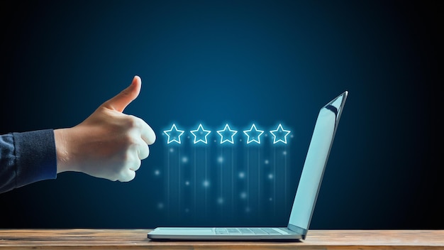 The concept of five stars The best rating on the Internet Hand showing thumbs up in front of laptop