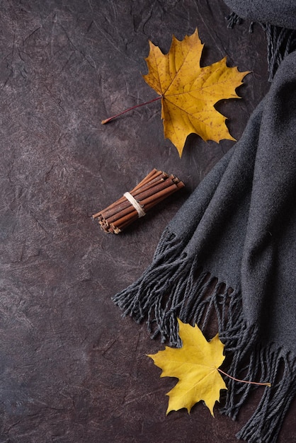 Concept flat lay with autumn maple leaves and a cozy gray scarf on a dark concrete background Top view and copy space