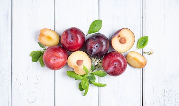 Concept flat lay with  juicy red plums and green leaves  on a white  wood background. Top view  image