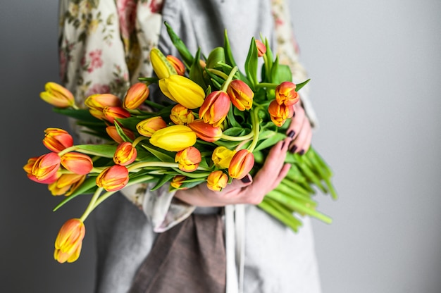 The concept of the florist's work. A girl holds a bouquet of yellow, orange and red Tulips. White background