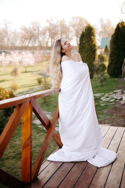 Concept good morning blonde woman on the balcony covered with white duvet morning woman portrait