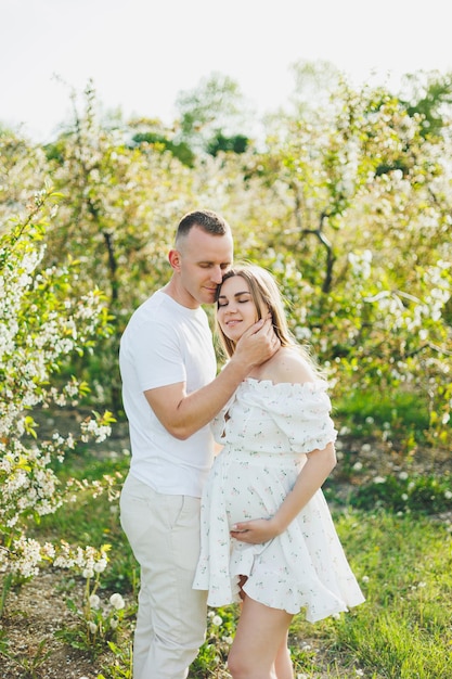 The concept of happy family relationships A young happy couple in anticipation of pregnancy walks through a blooming garden Couple in love in blossoming apple trees