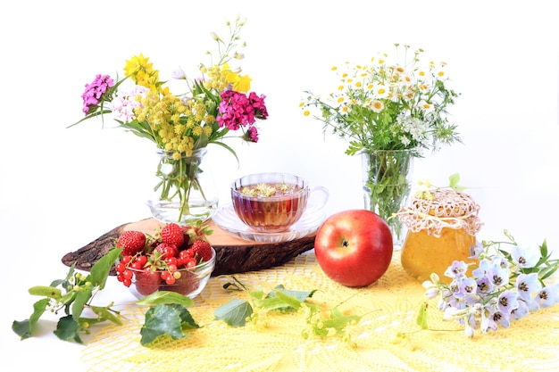 The concept of harvesting in the summer season Ripe berries and fruits a jar of jam lime branches on a yellow napkin light background side view