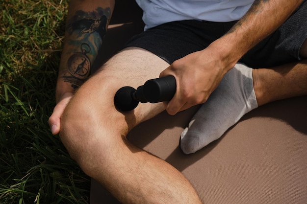 Concept of healthy lifestyle Caucasian man massages himself with percussion gun outside