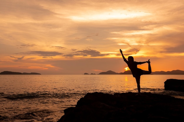 Concept healthy and relaxing with silhouette of young woman practicing yoga on the rock