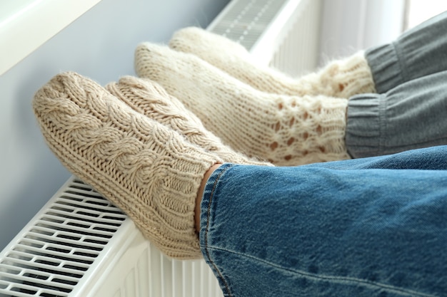 Concept of heating season with legs in knitted boots on radiator.