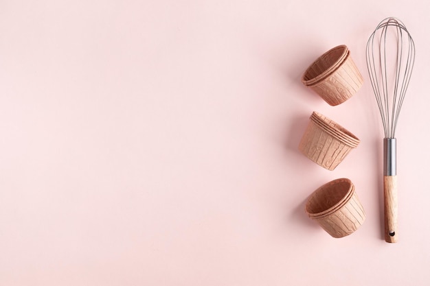 The concept of homemade baking is a whisk for whipping and cupcake molds on a pink background Zero waste Copy space Top view Baking concept flat lay