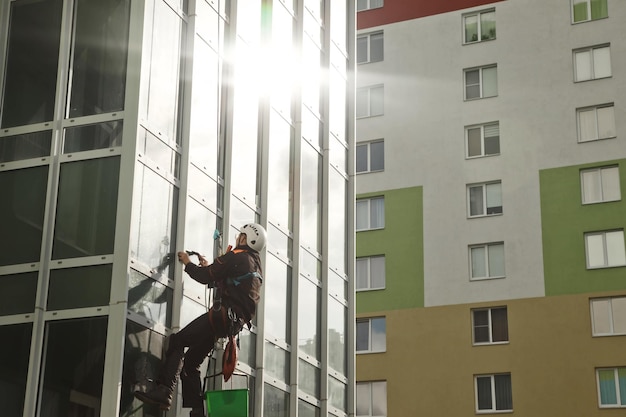 Concept of industry urban works Industrial mountaineering worker in uniform hangs over residential facade building