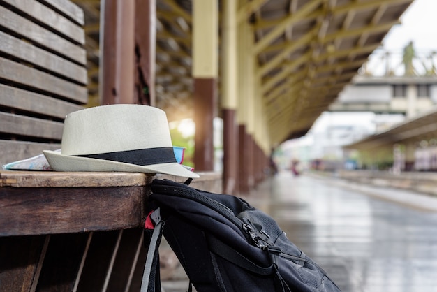 Concept life style holidays travel or journey : Old white hat with black backpack put on the wooden bench at the train station.