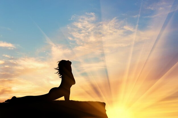 Concept of meditation and relaxation. Silhouette of a girl practicing yoga exercise on the sunset background