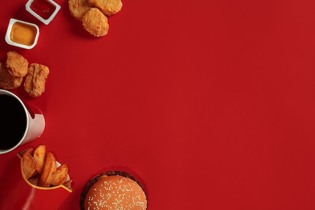 Concept of mock up burger potatoes sauce chicken nuggets and drink on red background copy space for ...