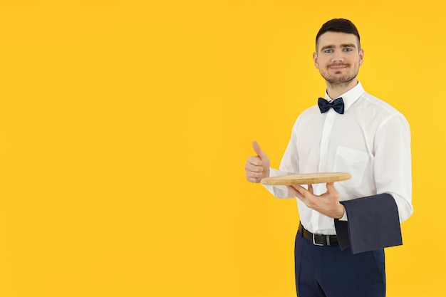 Concept of occupation young waiter on yellow background