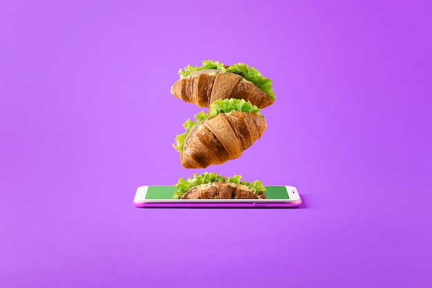 Concept of online food delivery with copy space Flying sandwiches from a smartphone on a purple background