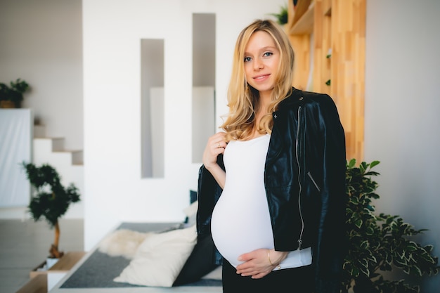 Concept - pregnant belly of caucasian blonde girl in white shirt in white light room