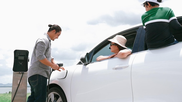 Concept of progressive happy family enjoying their time at wind farm with electric vehicle Electric vehicle driven by clean renewable energy from wind turbine generator for charging station