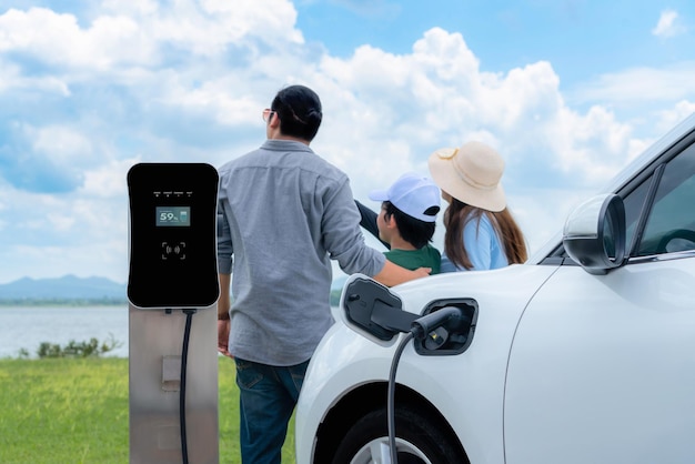 Concept of progressive happy family with EV car at natural outdoor scenic