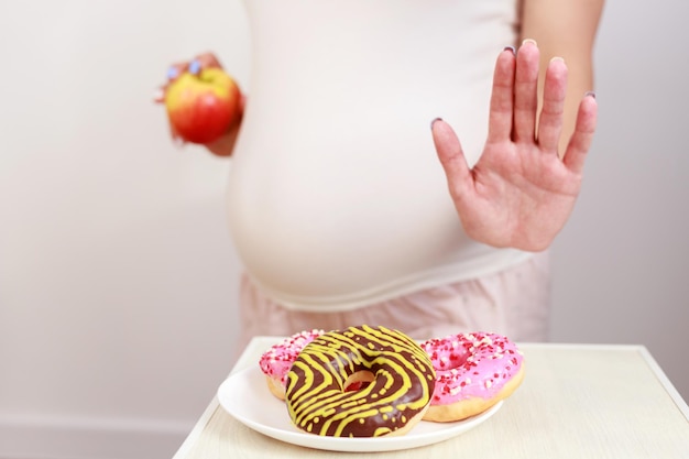 The concept of proper pregnancy nutrition pregnant woman with donuts and apple