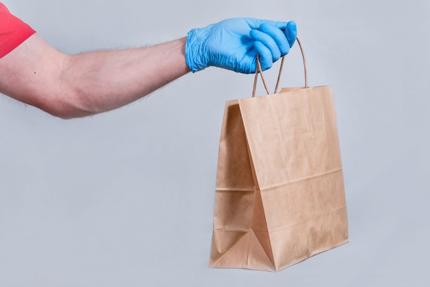 concept of safe delivery in close-up. courier's hand in protective medical gloves holds a paper bag. contactless delivery of orders