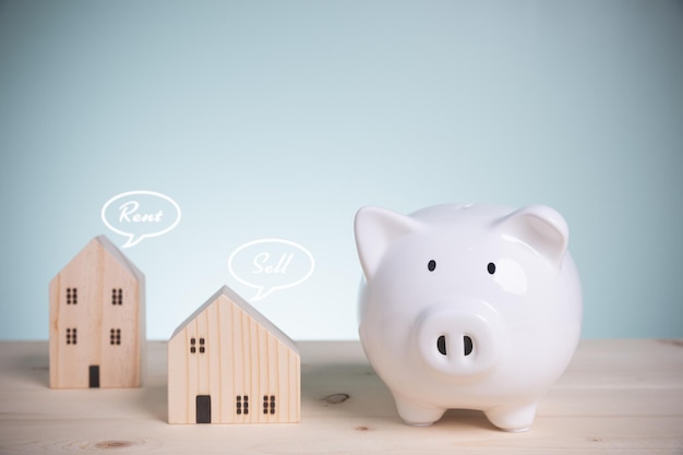 Concept save money loan and banking A single white piggy bank with house wood model on old wood with copy space on a green background For loans buy residential or homes to the future