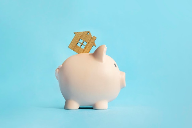 The concept of saving money to buy an apartment, house or other residential property. Piggy bank and wooden house on a blue background.