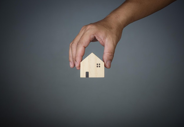 Concept of selling a house A hand is holding a model house on a gray background .